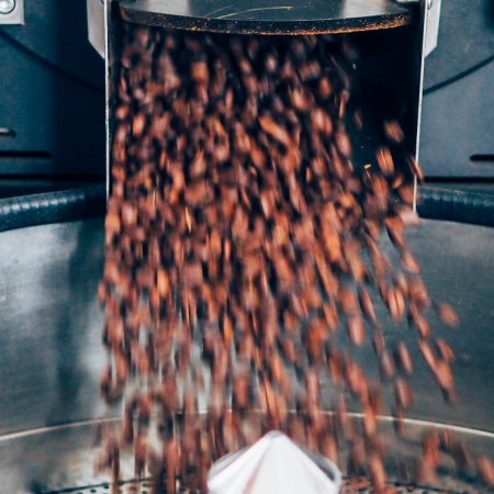 Granos de café recién tostados cayendo desde la tostadora industrial.